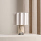 Table lamp with a white veined marble base and white fluted linen shade near sheer curtains