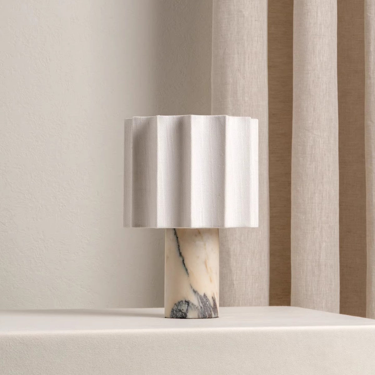 Table lamp with a white veined marble base and white fluted linen shade near sheer curtains