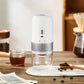 White electric coffee grinder on a table with coffee beans, a cup of coffee and a pour-over dripper