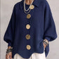 Woman in a navy loose knit top with a collar and large gold tone buttons, front view