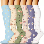 Six pairs of knee-high floral print compression socks in light blue, cream, green, peach, purple and white worn side by side