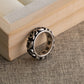 Scrollwork band ring tilted on a wooden tray corner showing the engraved lettering on the inner surface, on linen cloth