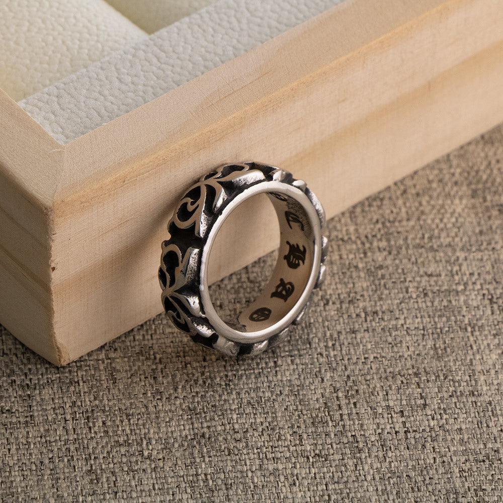 Scrollwork band ring tilted on a wooden tray corner showing the engraved lettering on the inner surface, on linen cloth