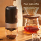 Black electric coffee grinder beside a pour-over dripper and glass server, grounds visible in the clear chamber
