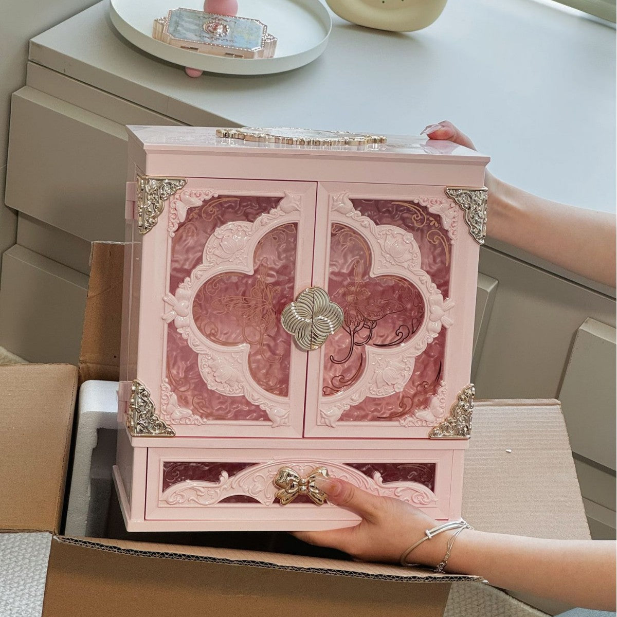 Peach pink makeup organizer cabinet without LED light, closed, held by a hand over an open shipping box