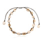 Cowrie shell choker on black cord on white, around fifteen shells laid face up in a ring