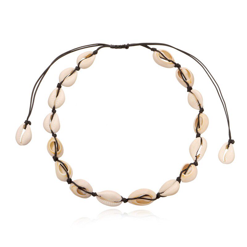 Cowrie shell choker on black cord on white, around fifteen shells laid face up in a ring