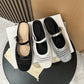 Black, off-white and silver woven mules seen from above on a white box beside a cream drawstring bag