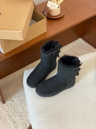 Black mid-height sheepskin boots with ribbon bows at the back on a cream pouf, Black Double Ribbon Thin Sole option, size 38