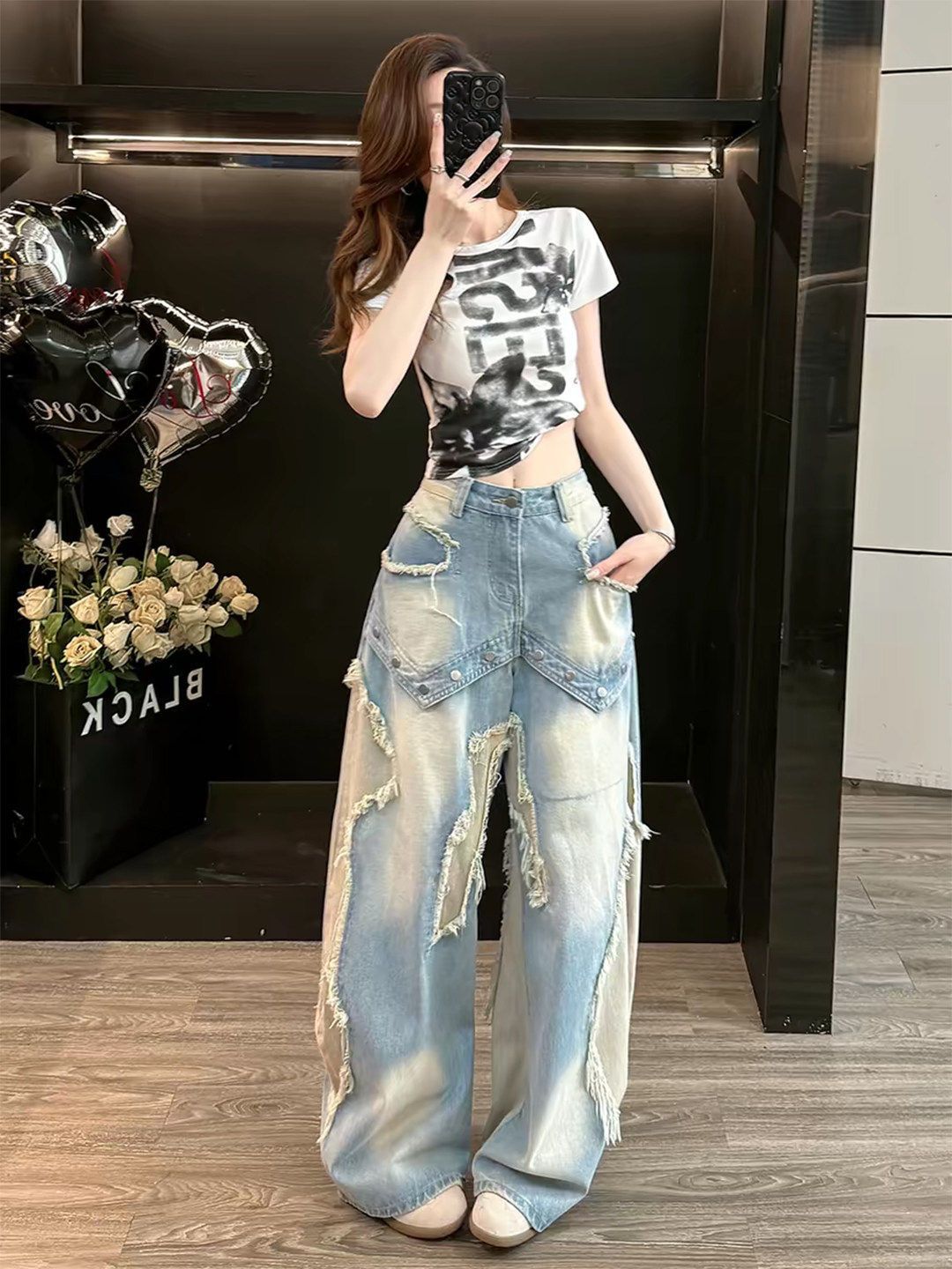 Woman in high waist wide leg washed blue baggy jeans with raw frayed star appliques, full length mirror view