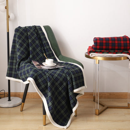 Navy and green tartan coral fleece blanket draped over a green chair with a cream pile edge