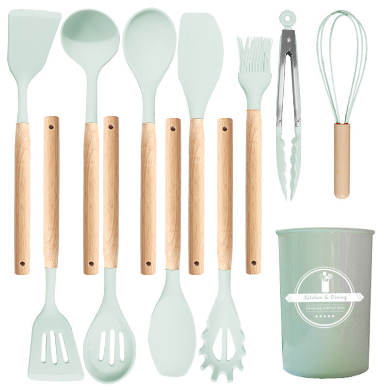 Light green silicone utensil set laid out flat with turners, spoons, ladle, brush, tongs, whisk and holder
