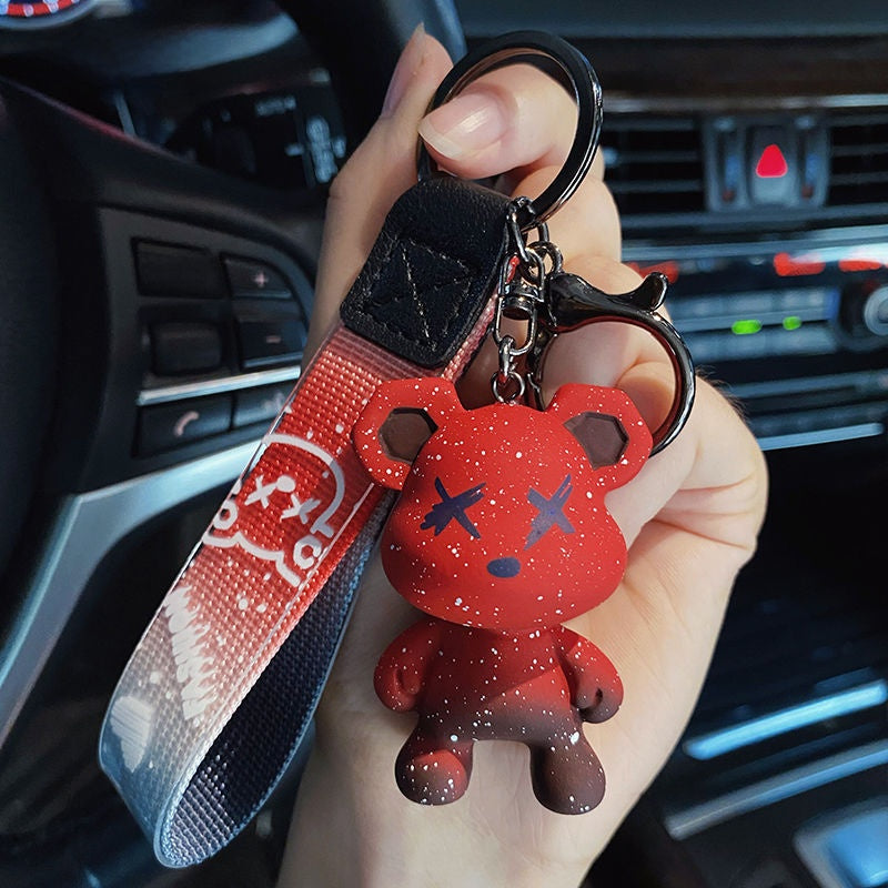 Bear keychain on a printed wrist strap clipped and held near a car dashboard