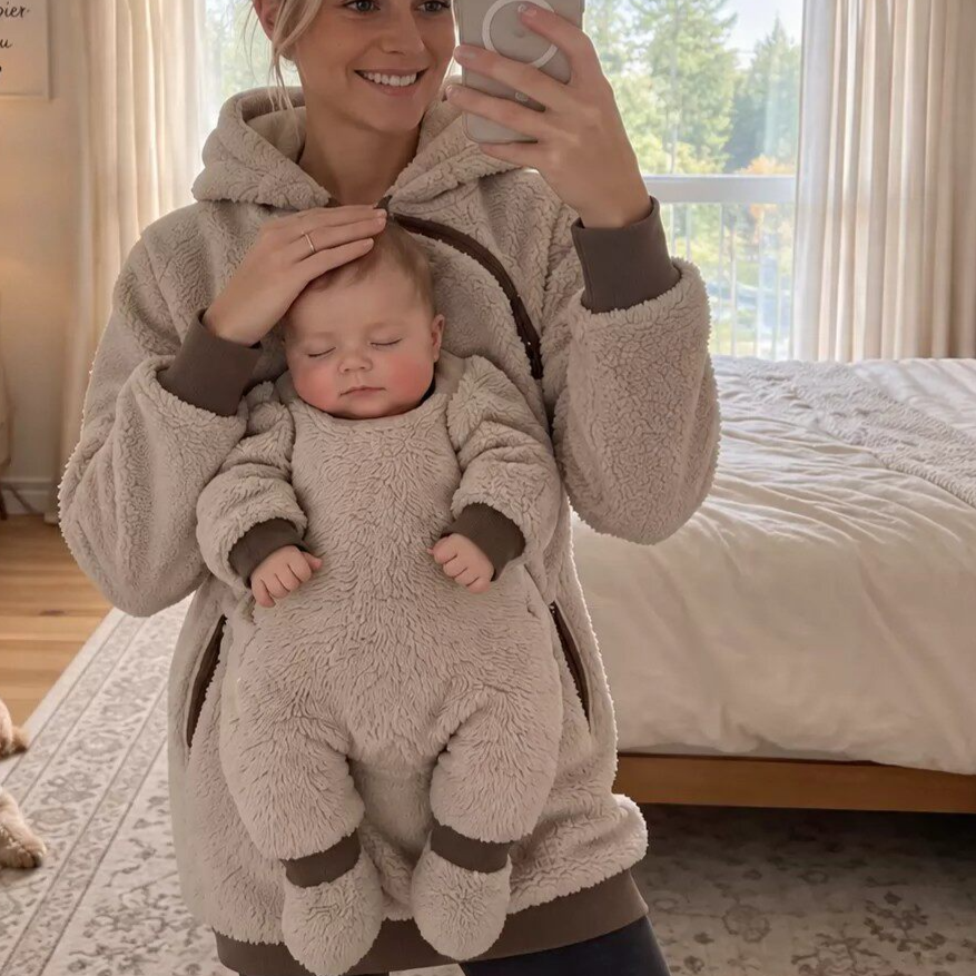 Beige teddy fleece hoodie with a baby asleep at the chest while the mother takes a mirror photo in a bedroom