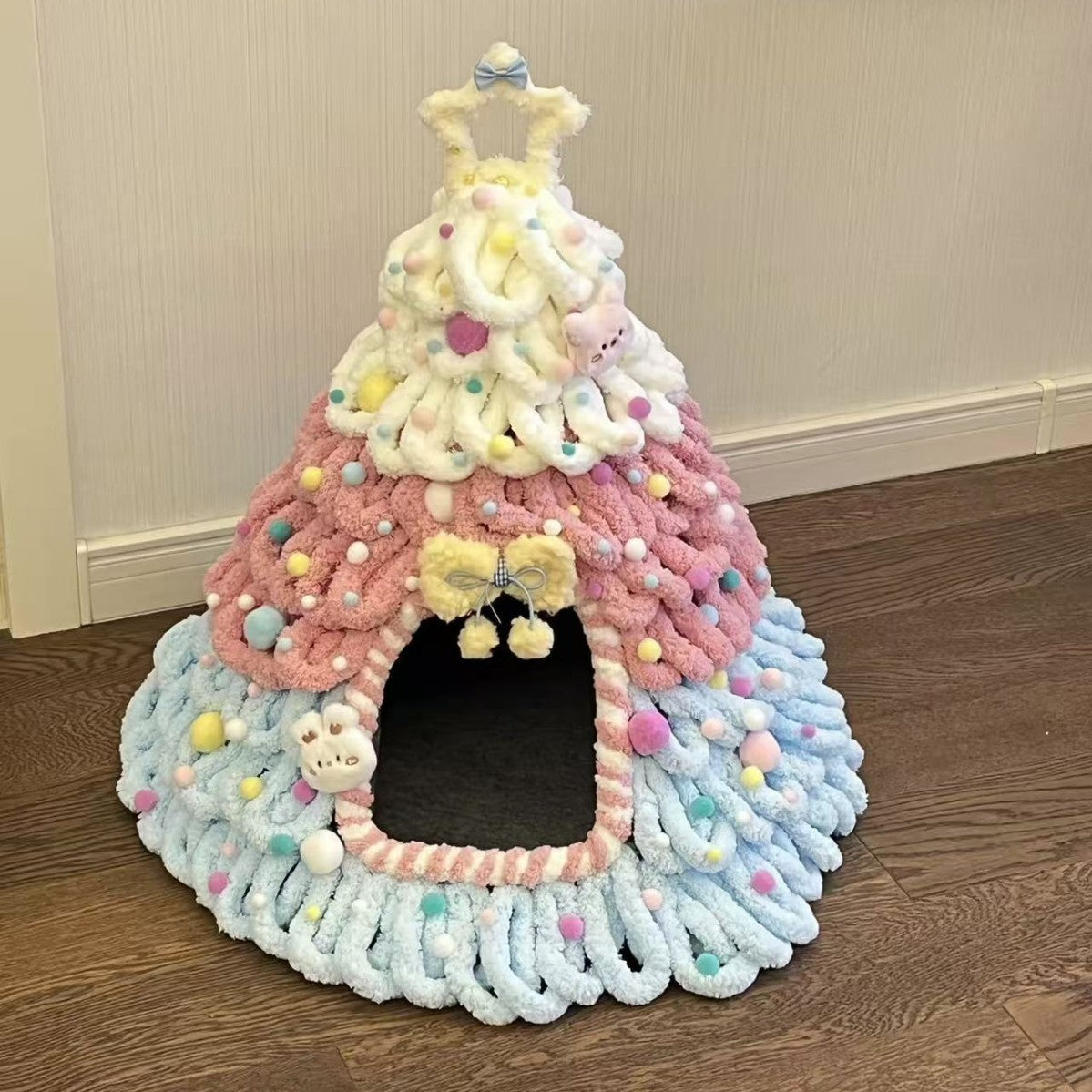 Pastel pink and blue chenille pet house with a yellow bow, a star outline on top and a dark doorway