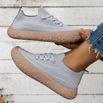 Pair of gray knit mesh slip-on sneakers with rose tan crackle-pattern soles held against a white wood wall
