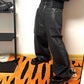 Black glossy waxed denim wide leg jeans worn indoors, the coated sheen catching light on the thigh