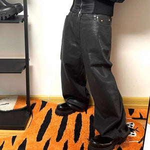 Black glossy waxed denim wide leg jeans worn indoors, the coated sheen catching light on the thigh