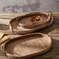 Two oval rattan trays on a wooden table, one holding pastries in a paper box, studded rim and handles