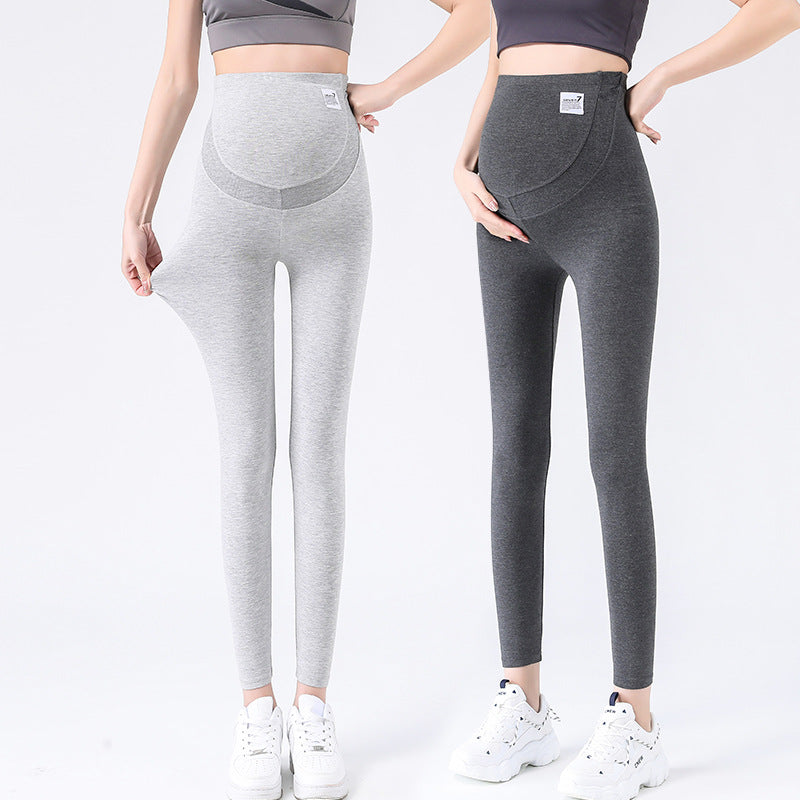 Two women in light gray and dark gray maternity leggings with belly panels, standing in white trainers