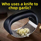 Rocking garlic press mincing peeled cloves into paste through the perforated plate on wood