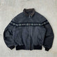 Charcoal washed collared jacket with a corduroy style collar and a woven band across the chest on a concrete floor