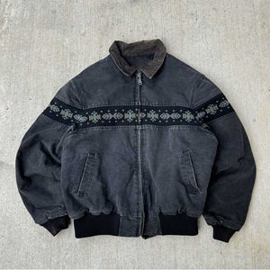 Charcoal washed collared jacket with a corduroy style collar and a woven band across the chest on a concrete floor