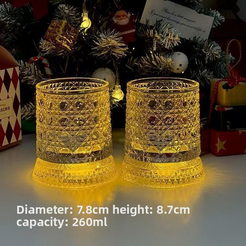 Two cut glass whiskey tumblers lit amber in front of a Christmas tree and wrapped gifts