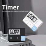 White and black plastic digital kitchen timers with large LCD displays in a styled grey scene