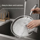 Hands washing a hammered flat pan under running tap water in a kitchen sink
