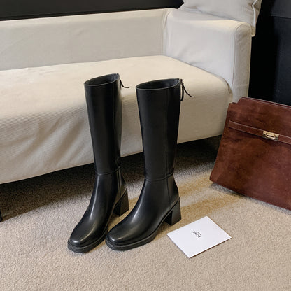Black cowhide leather tall riding boots with a block heel and round toe standing on carpet