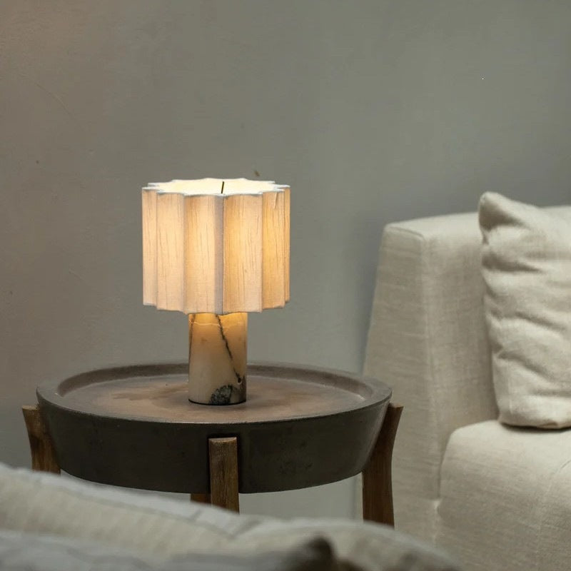 Marble table lamp lit on a dark round side table beside a linen sofa