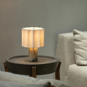 Marble table lamp lit on a dark round side table beside a linen sofa