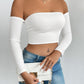 White stretch jersey crop top worn off the shoulder with long sleeves and a white belt on jeans