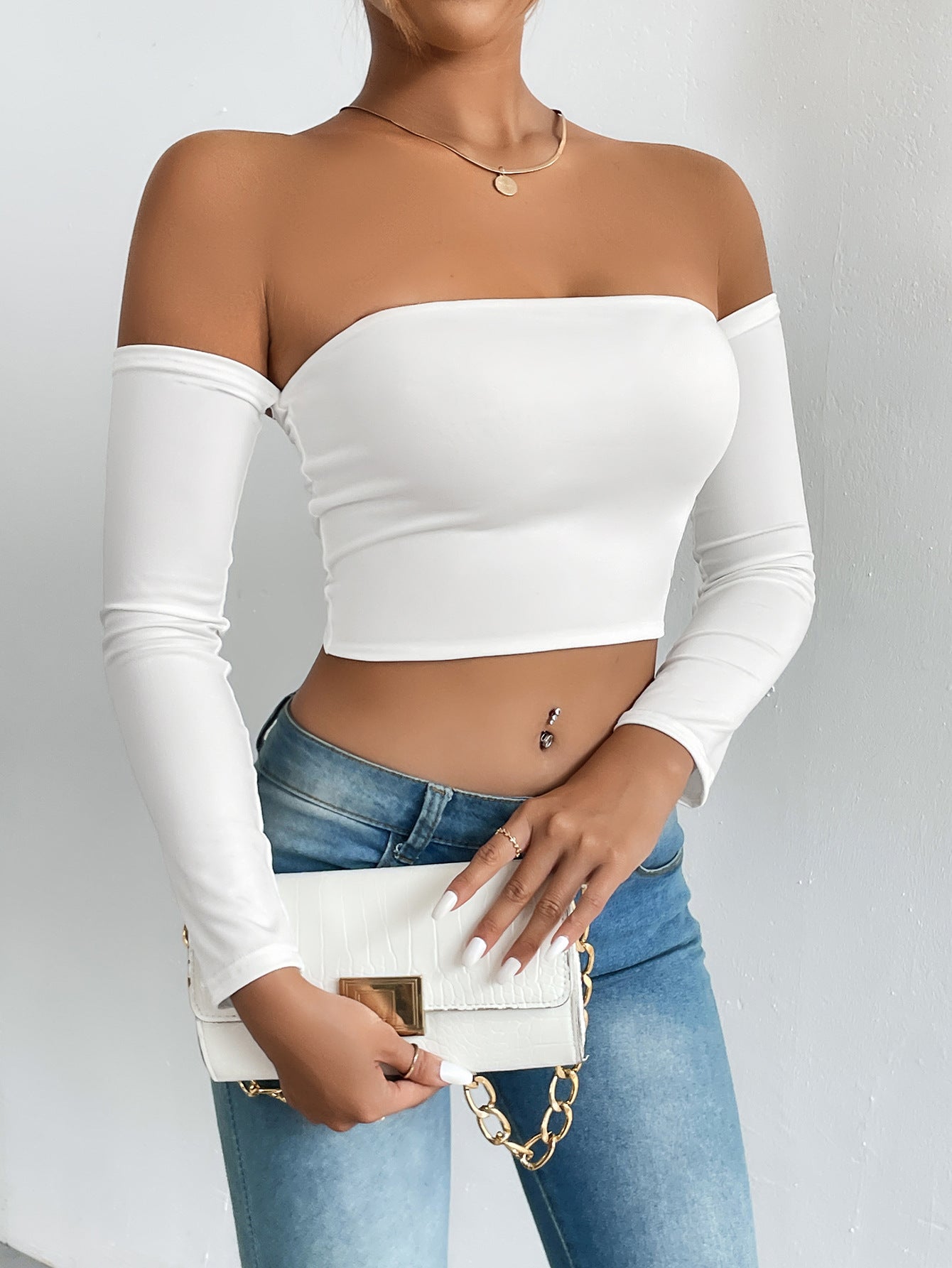 White stretch jersey crop top worn off the shoulder with long sleeves and a white belt on jeans