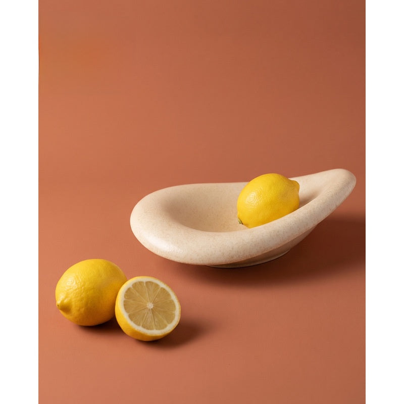 Glossy beige ceramic oval fruit bowl with lemons on a terracotta colored backdrop