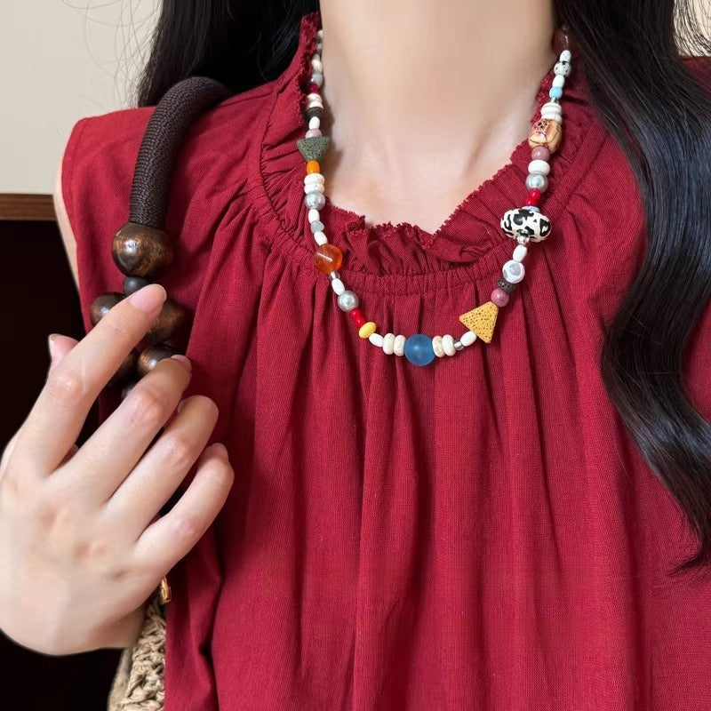 Multicolor beaded necklace with pearls and small charms worn over a red top