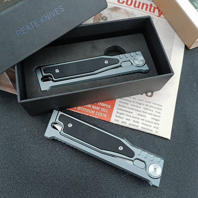 Two folding pocket knives, one in an open black box with foam and one lying beside it on a newspaper page