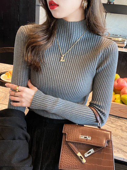 Woman wearing a grey slim ribbed semi high mock neck knit sweater with a gold necklace