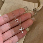Sterling silver double cross necklace with cubic zirconia held over a cotton pouch