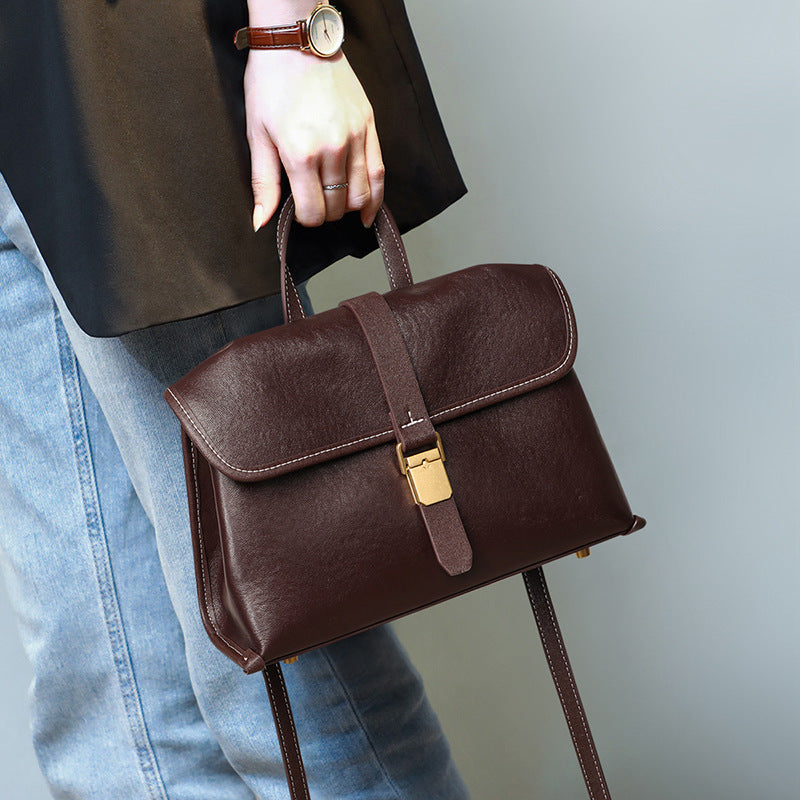Hand holding the coffee brown flap satchel by its handle beside blue jeans, Brown coffee option