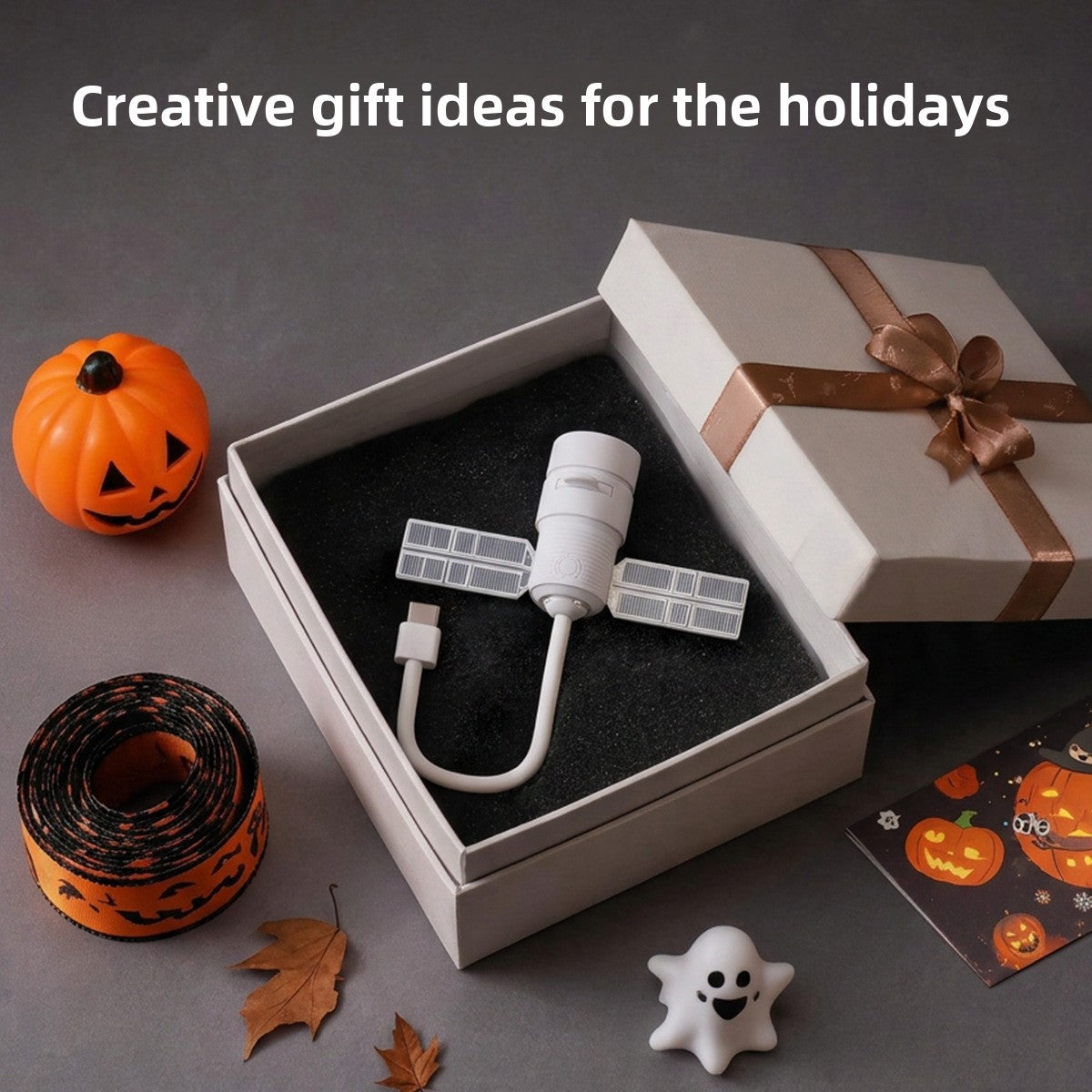 White projector with USB cable resting in an open gift box beside a pumpkin and Halloween ribbon