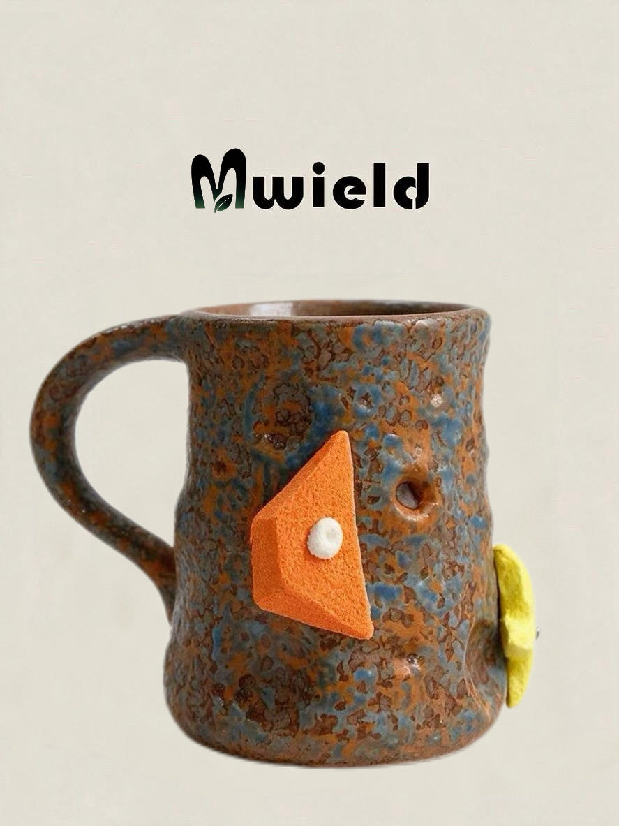 Brown and blue speckled ceramic mug with its handle on the left and an orange climbing hold decoration, side view