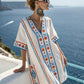 Loose V neck bohemian beach cover up dress in a blue and orange sun motif print, worn on a whitewashed terrace above the sea