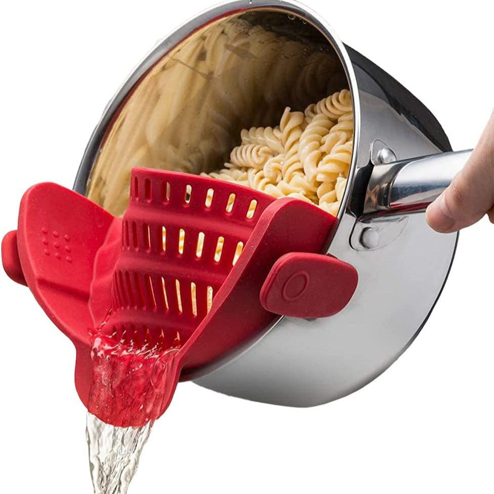 Red silicone clip-on pot strainer on a stainless steel pot draining pasta, water pouring from the spout