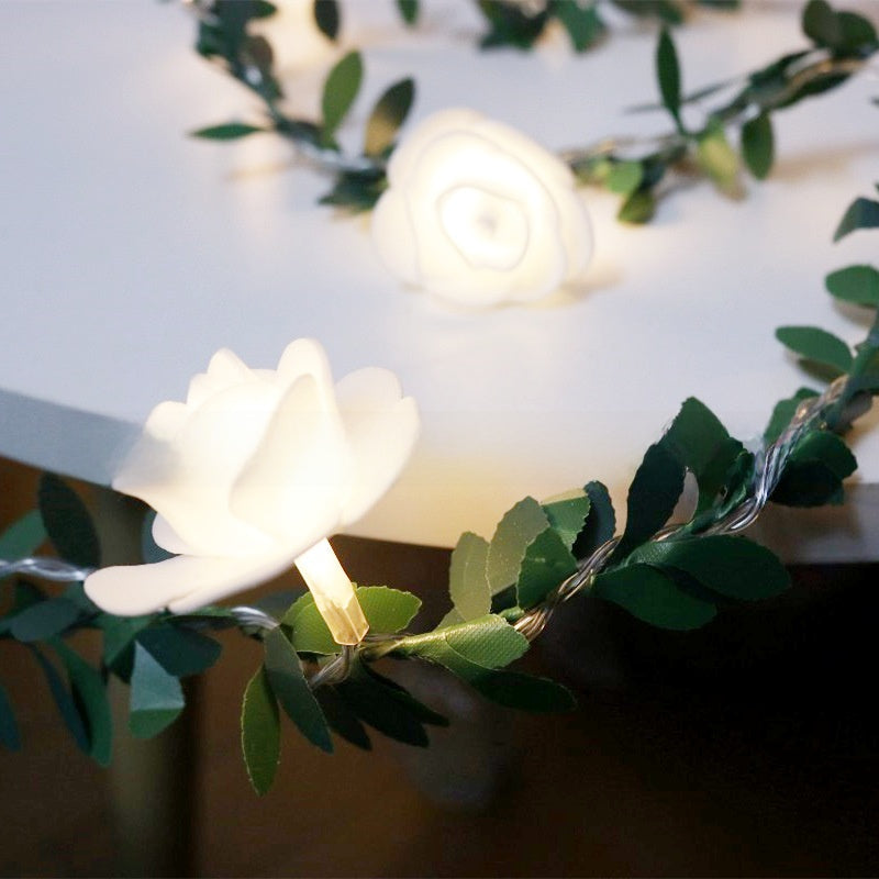 Decorative LED flower fairy string lights on a green leaf vine glowing warm, lifestyle photo