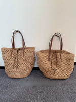 Large woven straw tote bag shown from the front with two long shoulder straps and an open top