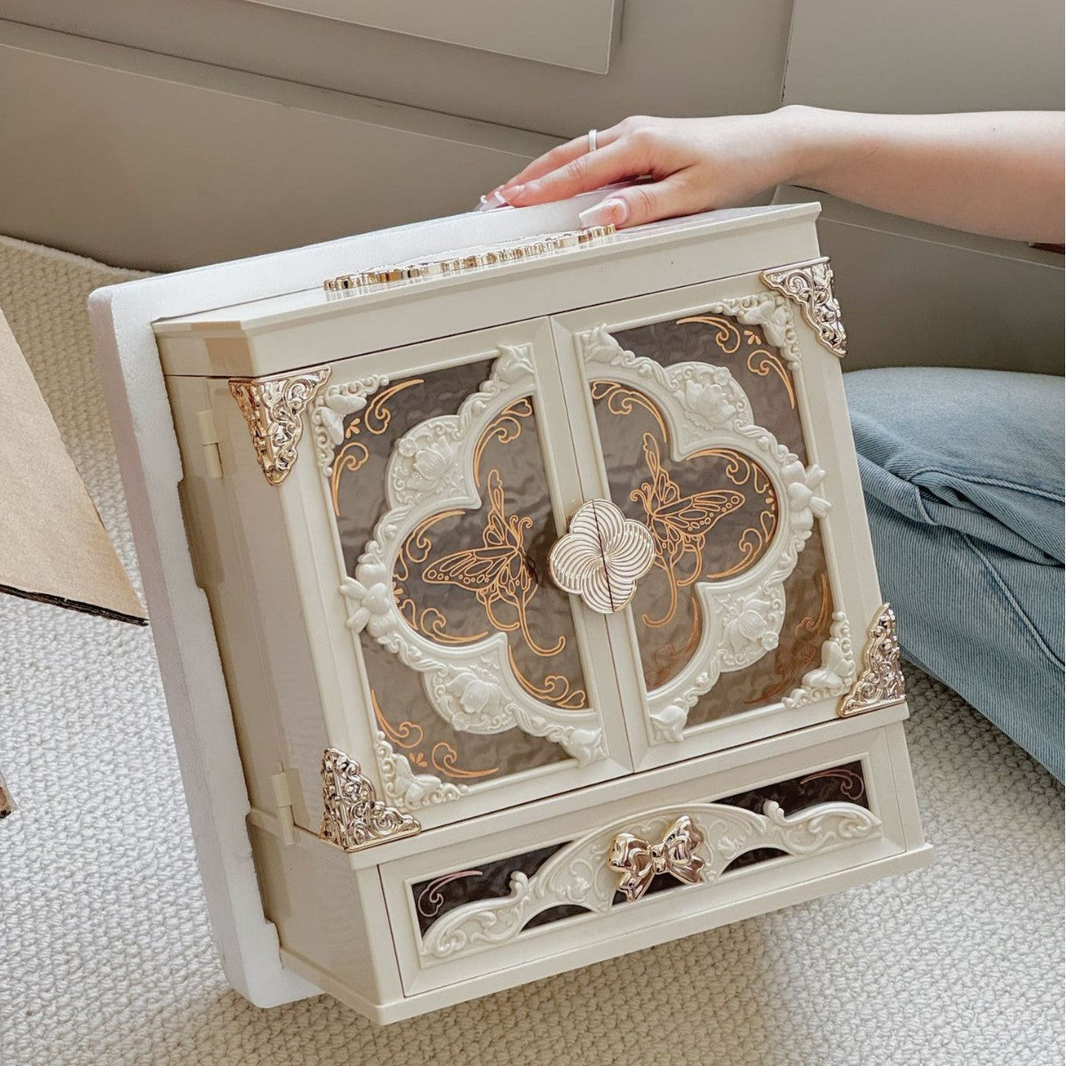 Ivory white makeup organizer cabinet without LED light, closed, held up by a hand in a room