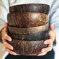 Hands holding a stack of natural coconut shell bowls with scratched dark brown outsides