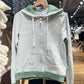 Green striped zip-up hoodie on a hanger showing the front pocket, drawstrings and green ribbed hem